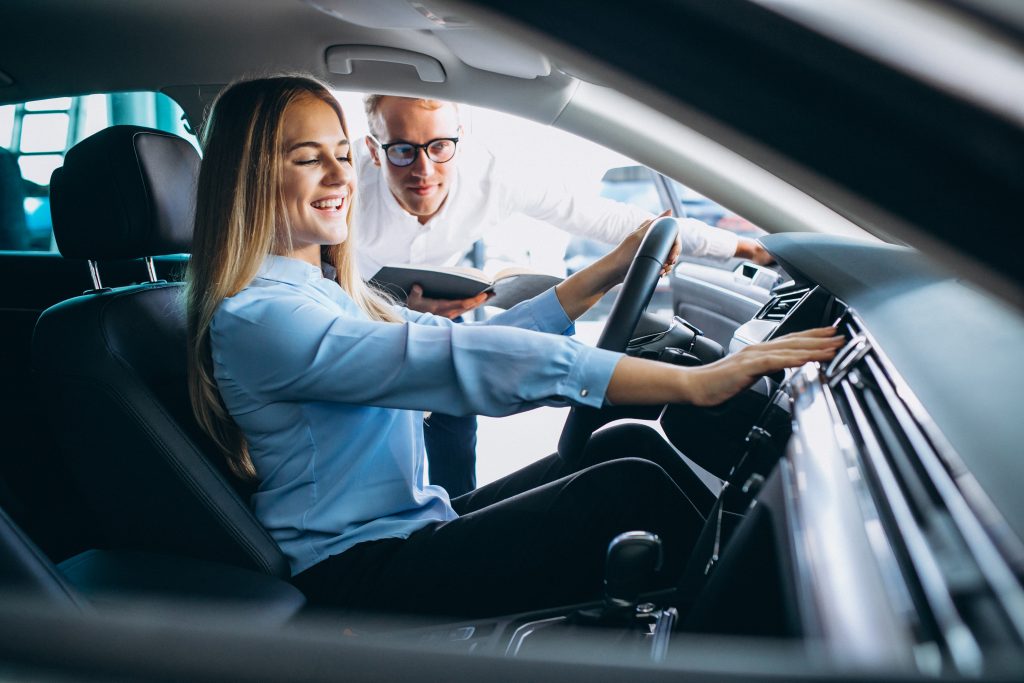 A woman sitting in the driver seat while another person helps checks a maintenance checklist over her vehicle. - Dann's Discount Auto Sales Visalia, CA