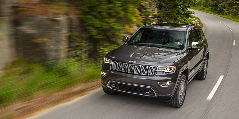 A dark colored 2021 Jeep Grand Cherokee cruising along a mountainous back highway. - Dann's Discount Auto Visalia, CA