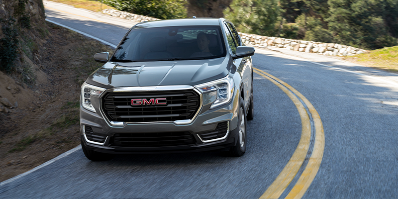 A silver 2023 GMC Terrain driving suburban backroads. - Dann's Discount Auto Sales Visalia, CA