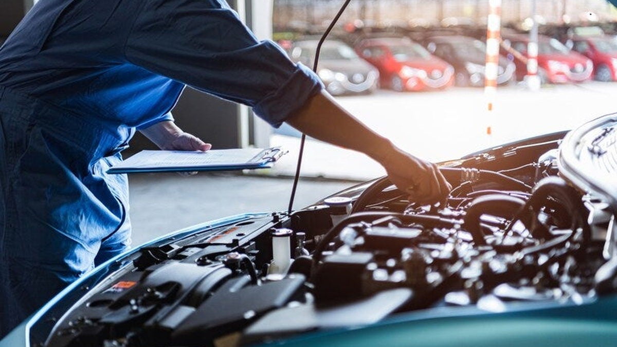 Technician inspecting the engine bay of a high mileage used car at Dann's Discount Auto Sales service department in Tulare CA